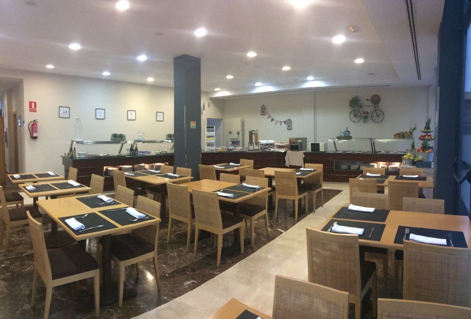 A restaurant with multiple tables and chairs, a counter with a display case, and a wall-mounted bicycle.