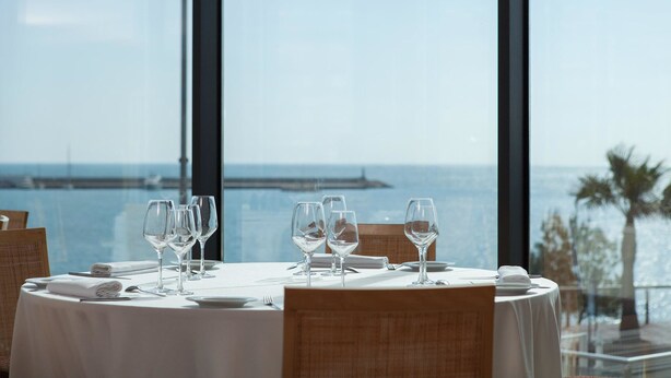 Una mesa de comedor preparada para cuatro, con vista al mar y un muelle al fondo.