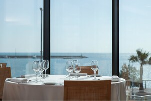 Una mesa de comedor preparada para cuatro, con vista al mar y un muelle al fondo.