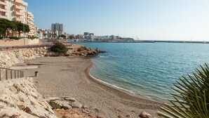 Un paisaje urbano costero con playa arenosa, costa rocosa y edificios al fondo.