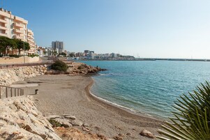 Un paisaje urbano costero con playa arenosa, costa rocosa y edificios al fondo.