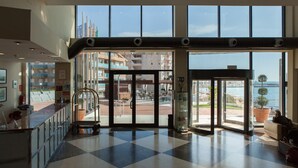 Un vestíbulo de hotel con mostrador de recepción, puerta de cristal de entrada y vistas a la ciudad y al agua.