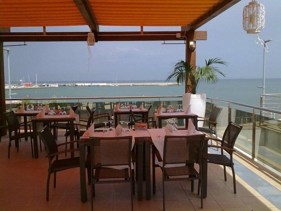 Un área de comedor al aire libre con mesas y sillas, con vista a un puerto deportivo y al mar.