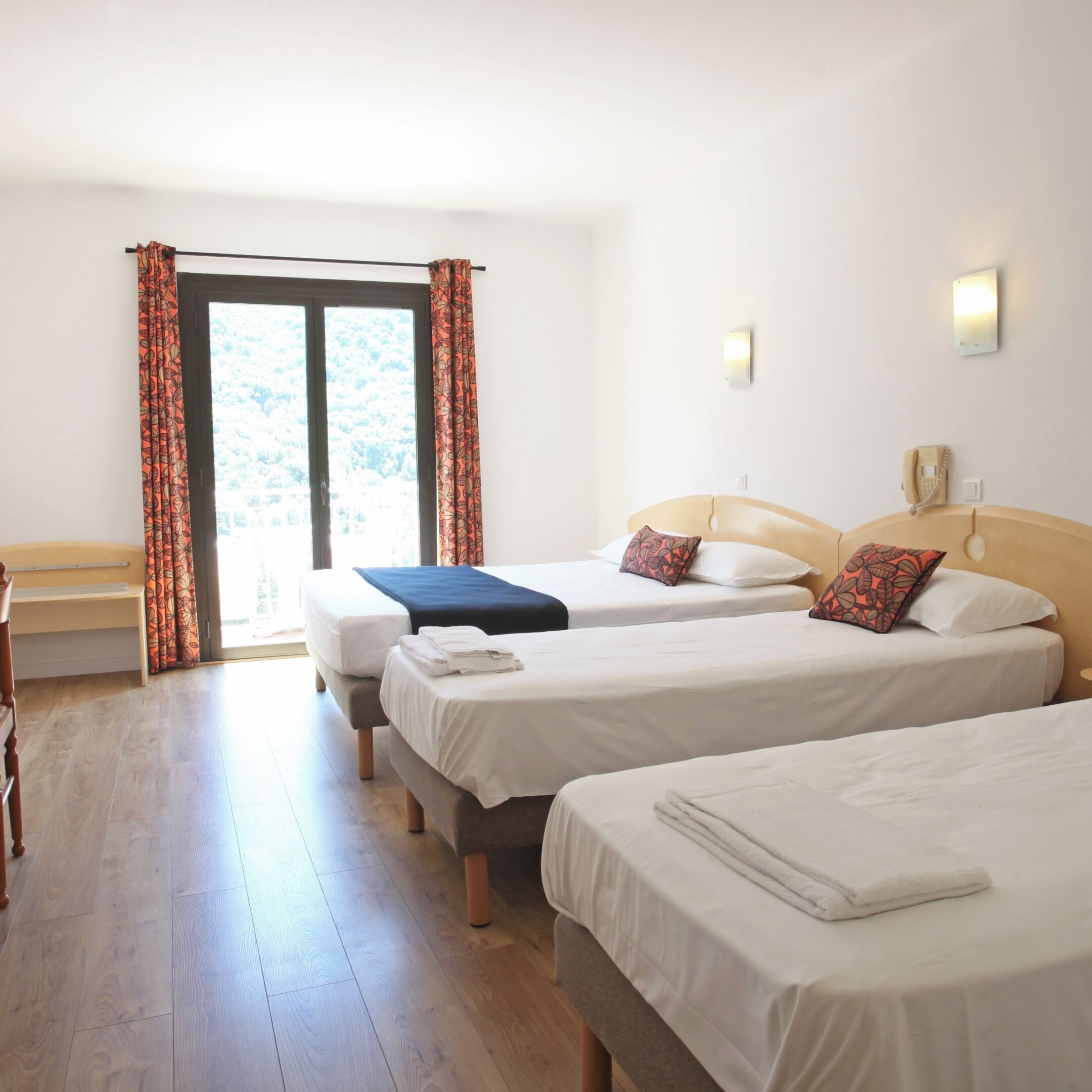 A hotel room with three beds, a bench, a desk, and a phone.
