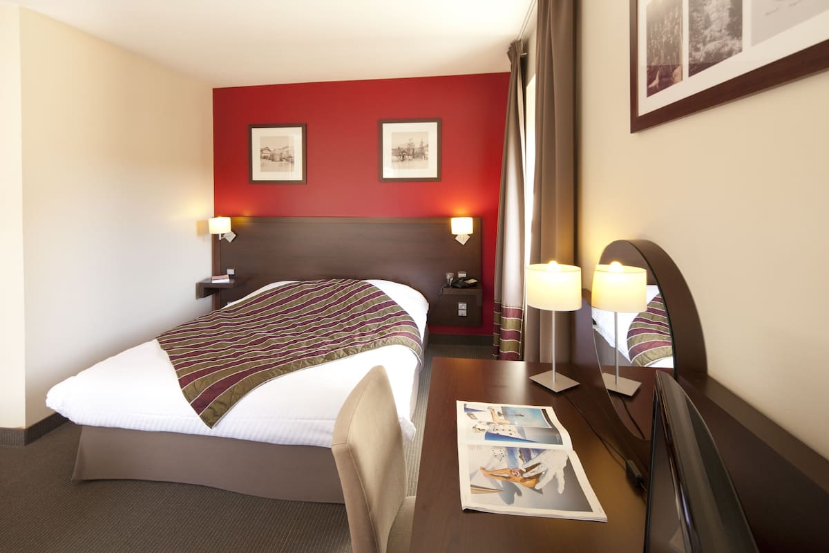 Een hotelkamer met een bed, nachtkastjes, een bureau met lamp en wanddecoratie.