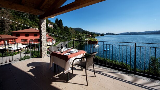 Une terrasse avec une table dressée pour le dîner, donnant sur un lac où l’on aperçoit des bateaux et des maisons au loin.