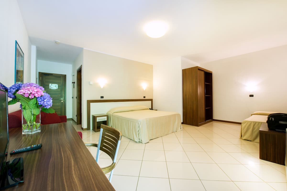 Een hotelkamer met een bed, nachtkastje, stoel en bureau met een bloevas.