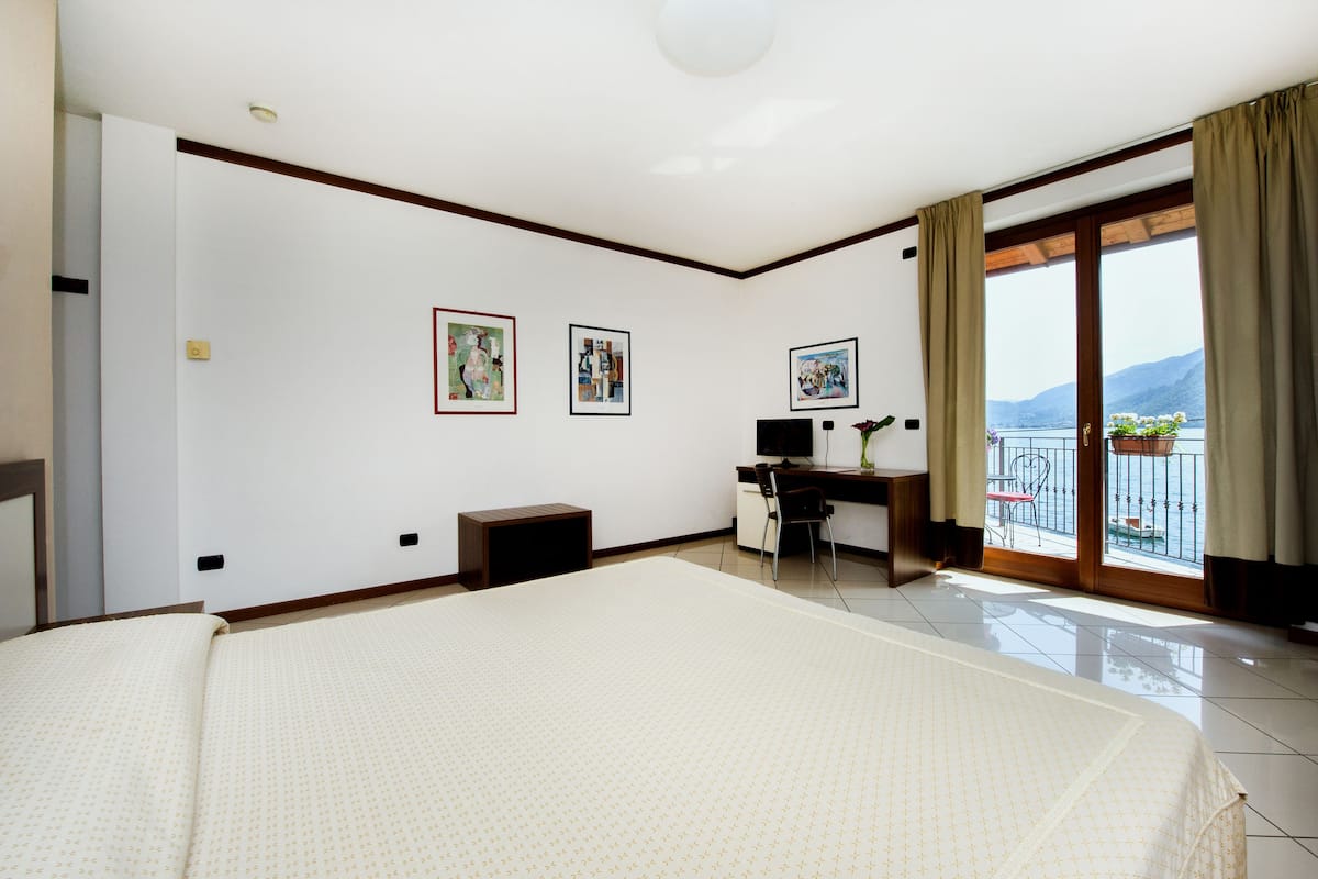 Een hotelkamer met een groot bed, een bureau met een computer, twee ingelijste foto's aan de muur en een balkon met uitzicht op de bergen.