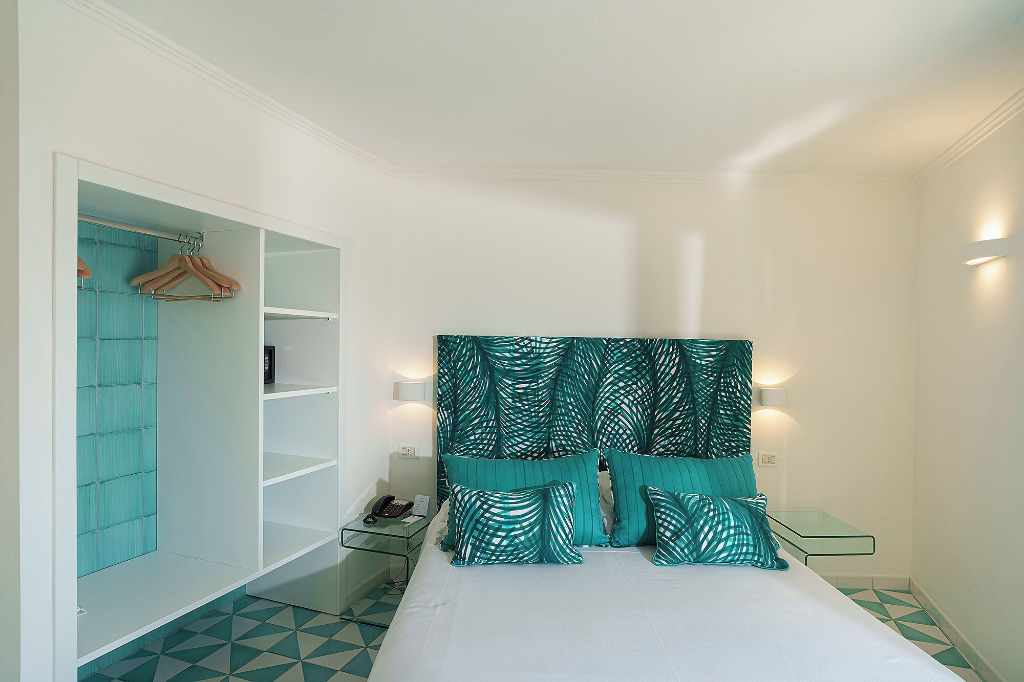 Un dormitorio con cama, armario, mesita de noche con lámpara y cortina estampada.