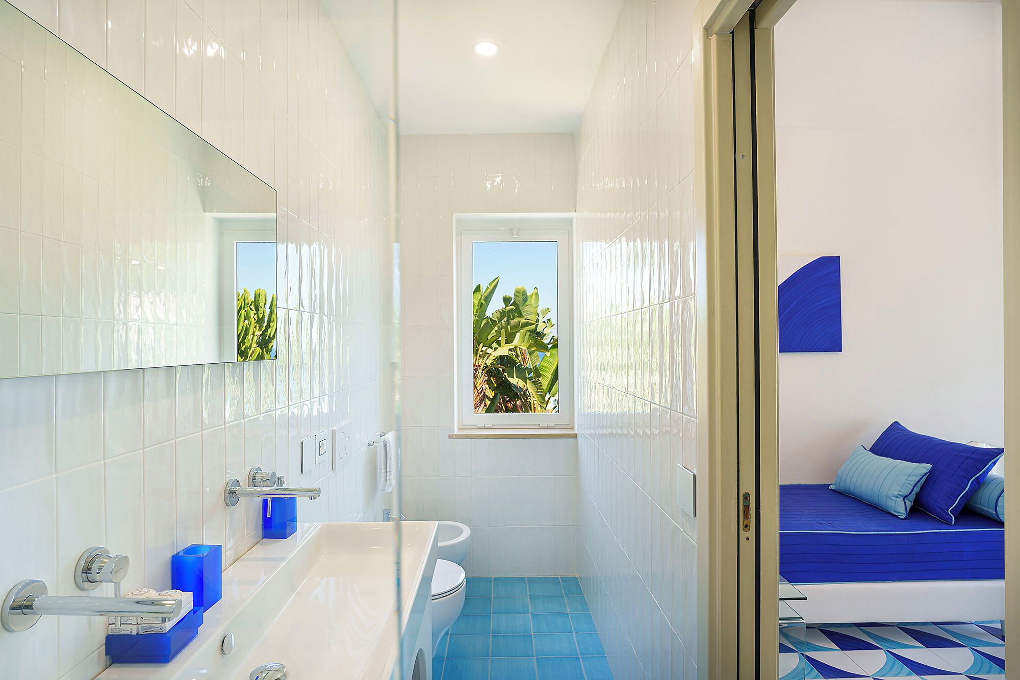 Une salle de bain avec une baignoire, un lavabo et des toilettes. Il y a une fenêtre donnant sur un espace verdoyant.