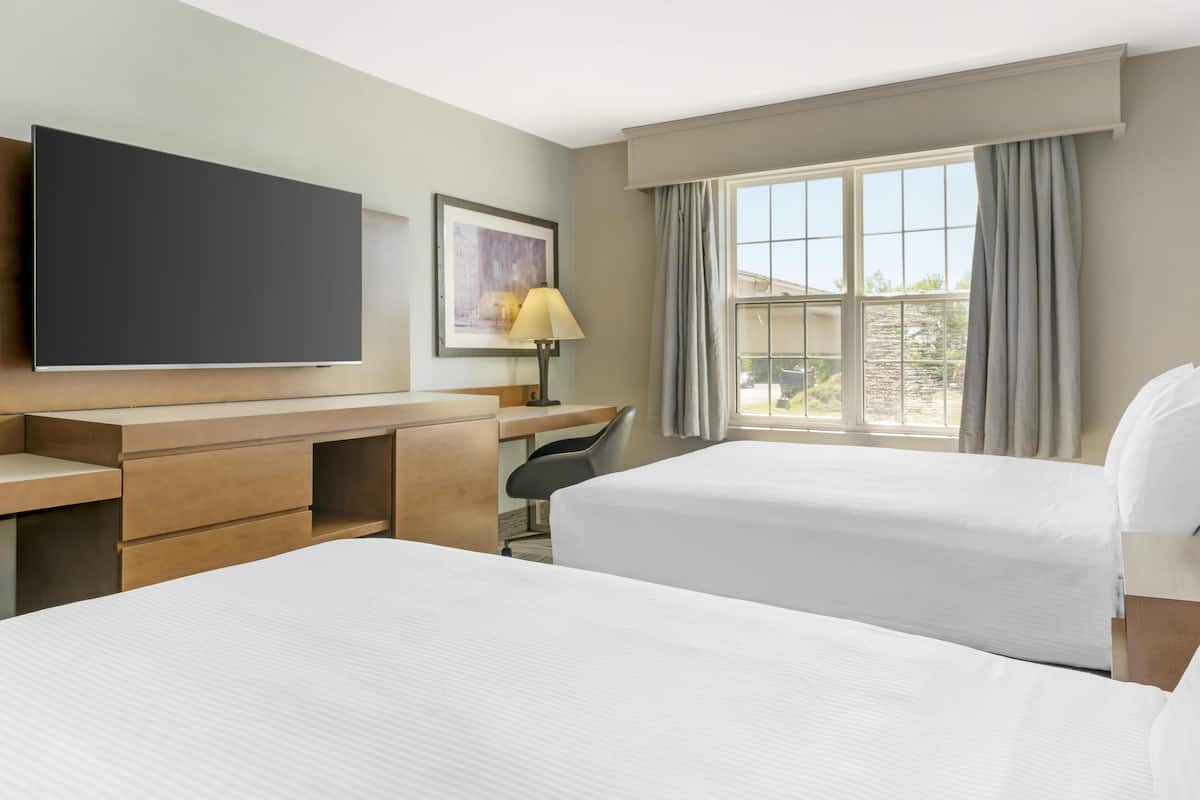 A hotel room with two beds, a desk, a chair, a TV, and a window with curtains.