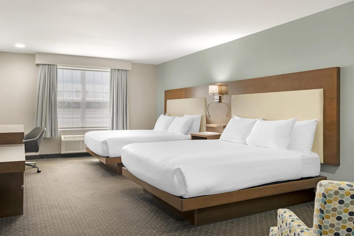 A hotel room with two beds, a desk, a chair, and a large window with curtains.