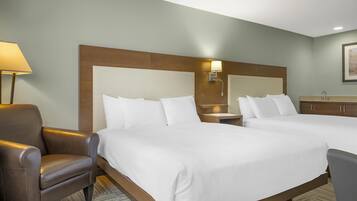 A hotel room with two beds, a brown leather chair, a nightstand with a lamp, and a wooden headboard.
