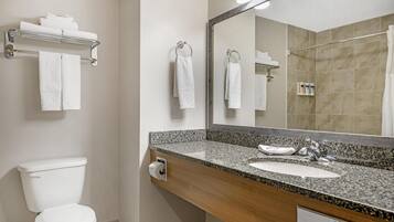 A bathroom with a toilet, sink, and a large mirror. There are towels hanging on a rack and a shelf above the sink.