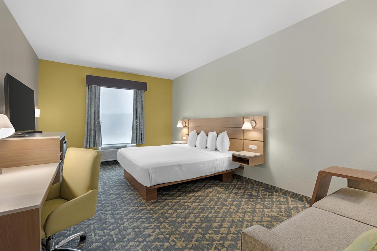 Une chambre d’hôtel avec un lit, un bureau, une chaise, un canapé et une fenêtre avec des rideaux.