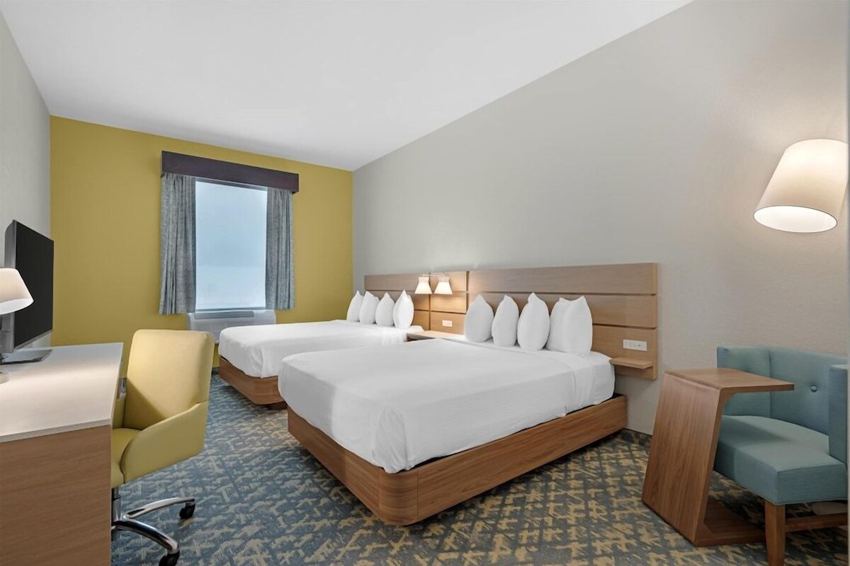Ein Hotelzimmer mit zwei Betten, einem Schreibtisch, einem Stuhl und einem Fernseher.
