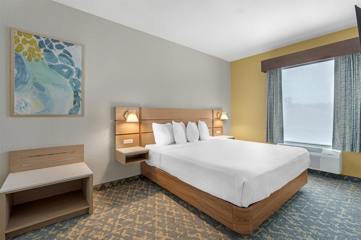 Ein Hotelzimmer mit einem großen Bett, Nachttischen, einem Schreibtisch und einem Fenster mit Vorhängen.