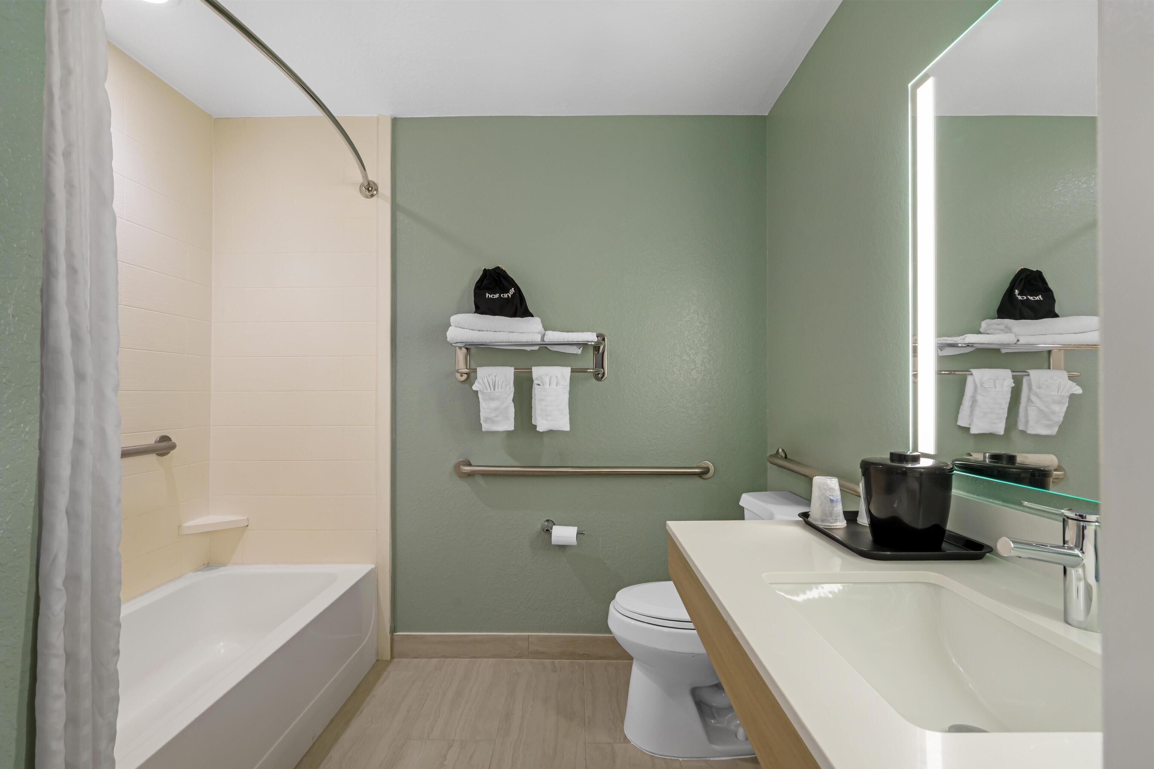 A modern bathroom with a bathtub, toilet, and sink. There are towels and a trash bin visible.