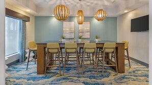 Une salle de conférence avec une longue table, six chaises, trois lampes suspendues, deux œuvres d’art encadrées et un téléviseur à écran plat fixé au mur.