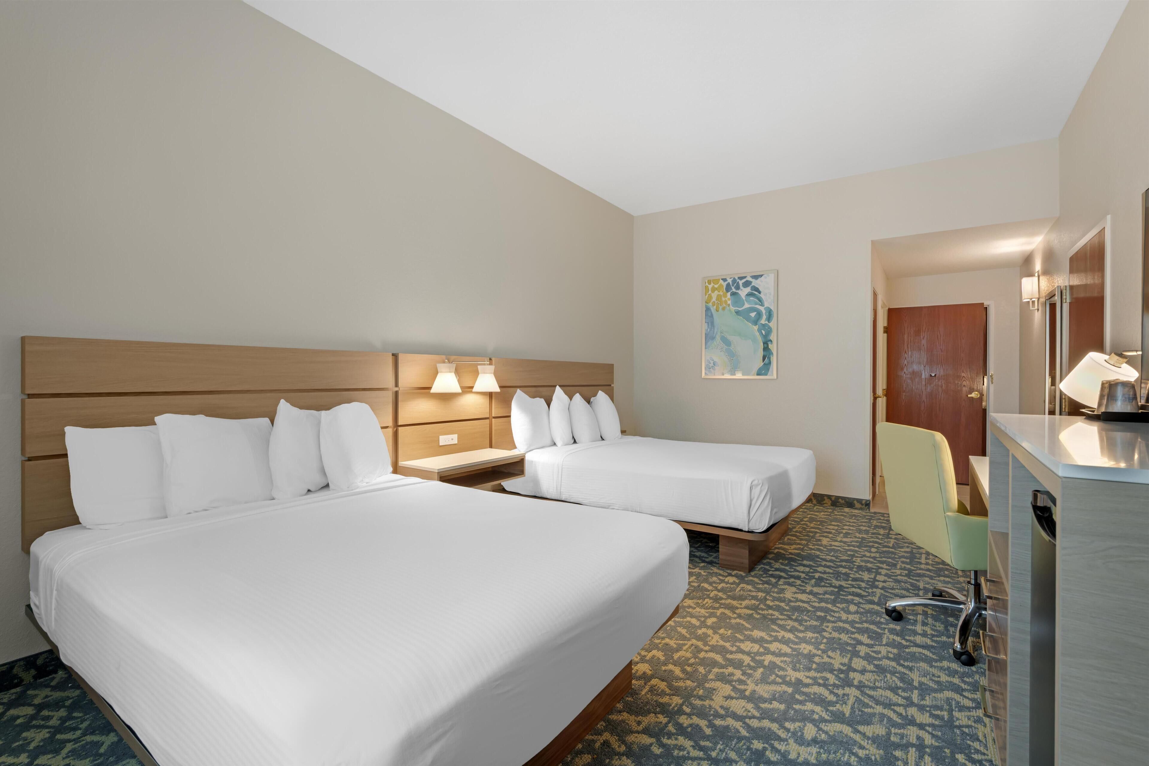 A hotel room with two beds, a desk, a chair, and a bathroom.
