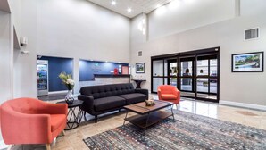 A spacious lobby with a black sofa, red armchairs, a coffee table, and a reception desk.