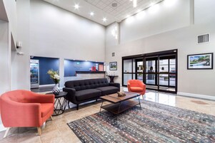 Un hall amplio con un sofá negro, sillones rojos, una mesa de centro y un mostrador de recepción.