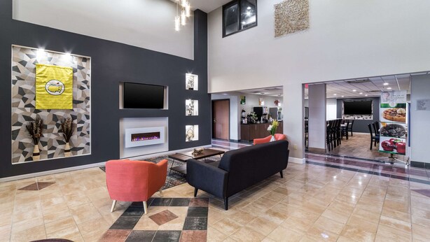 A modern lobby with a fireplace, seating area, and a kitchen visible in the background.
