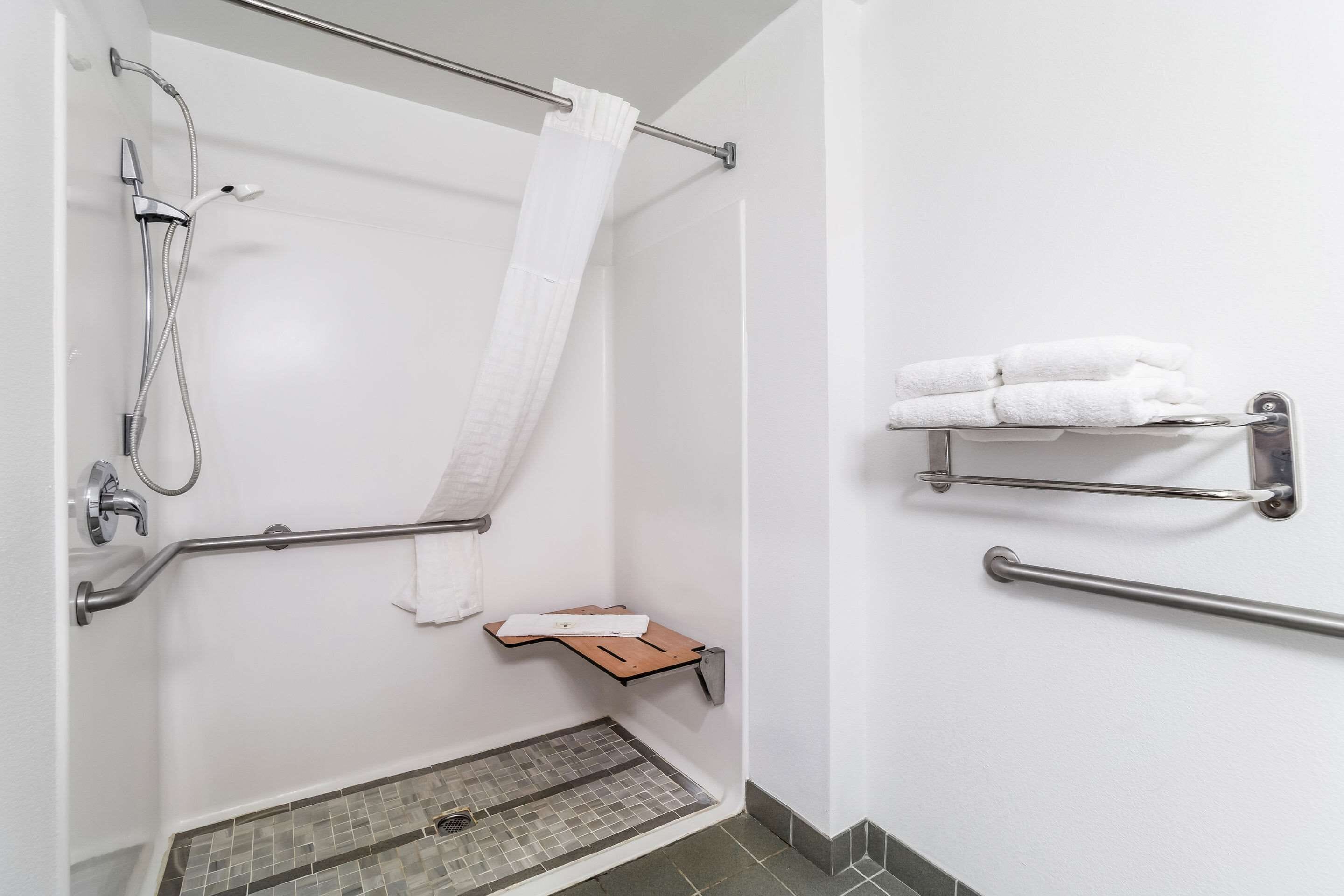 Un bagno con doccia, maniglie di sostegno, portasci e una piccola mensola in legno.