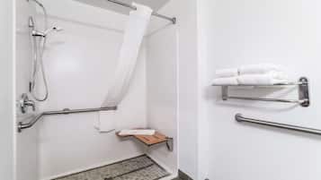 Een badkamer met een douche, handgrepen, een handdoekhouder en een klein houten plankje.