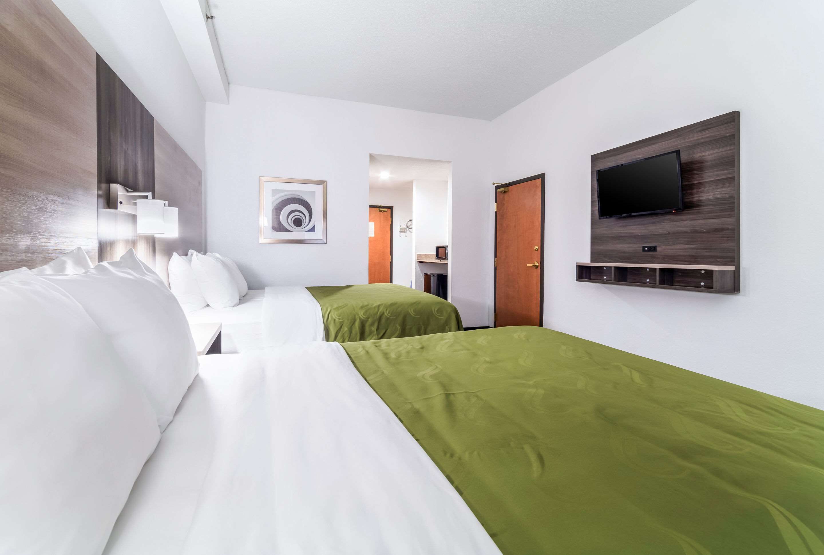 A hotel room with two beds, a TV mounted on the wall, and a painting on the wall.