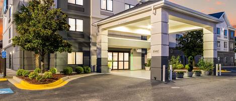 A modern hotel entrance with a covered driveway, a clear handicap parking sign, and a well-maintained landscaped area.