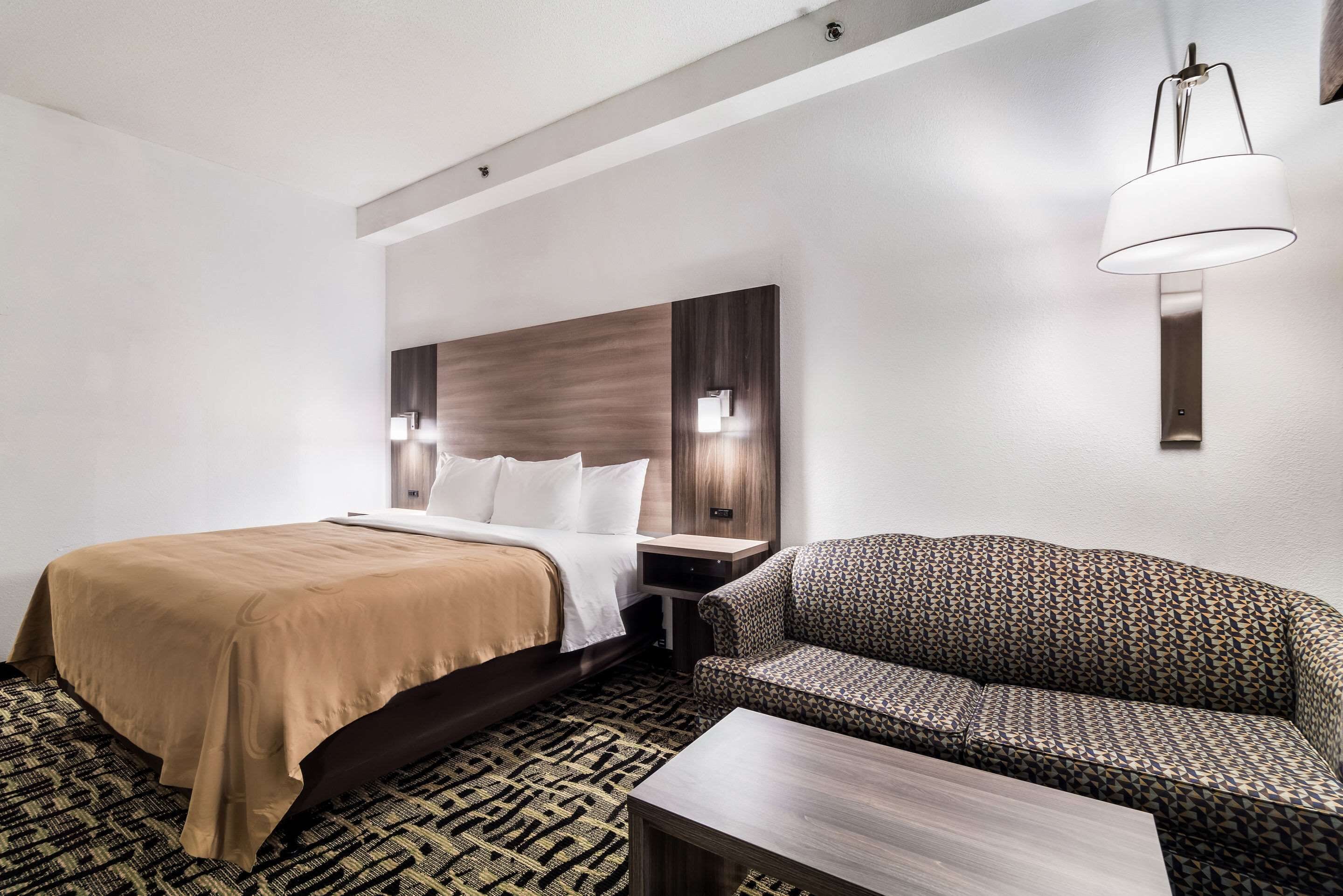 A hotel room with a bed, a sofa, a nightstand, and a lamp.