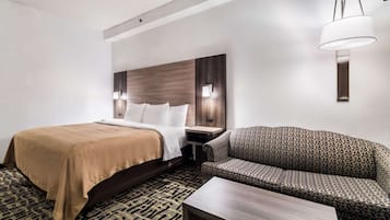 A hotel room with a bed, a sofa, a nightstand, and a lamp.
