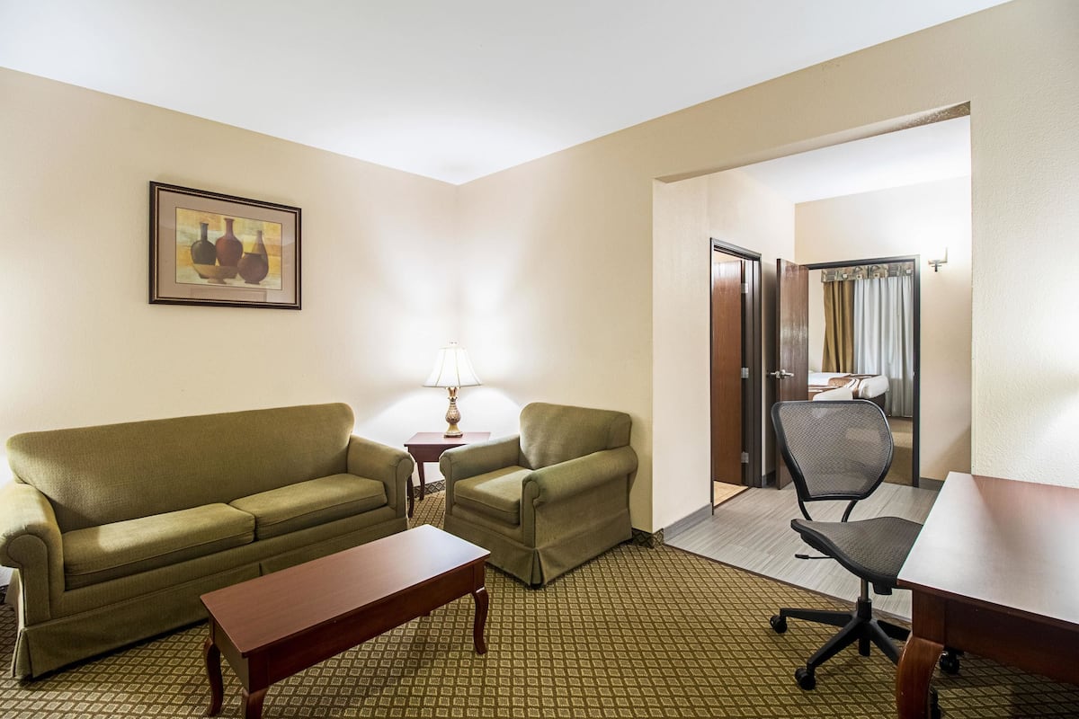 A hotel room with a green sofa, a small table, a lamp, a chair, and a desk.