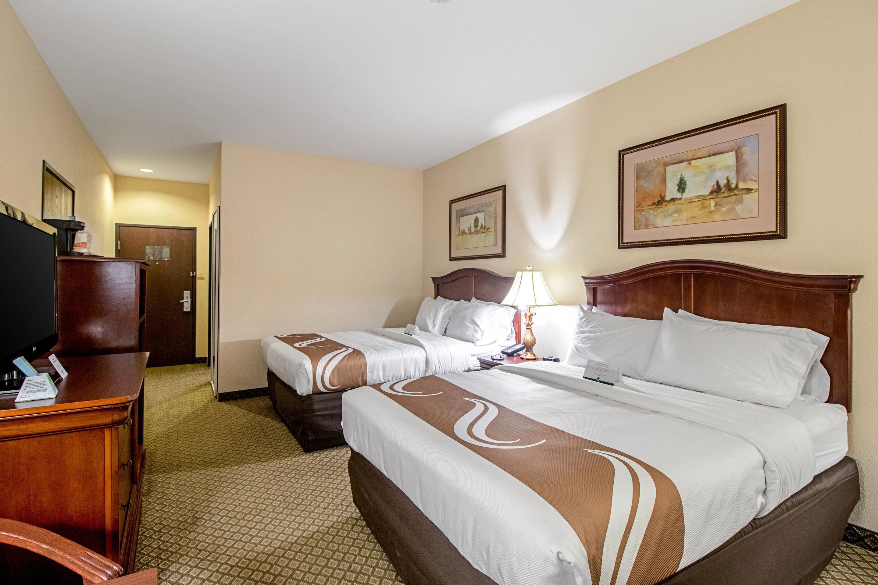 A hotel room with two beds, a desk, a television, and artwork on the walls.