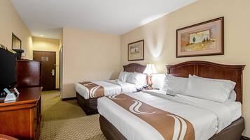 A hotel room with two beds, a desk, a television, and artwork on the walls.