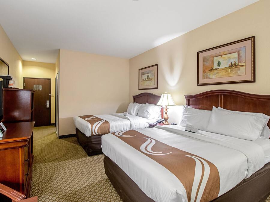 A hotel room with two beds, a desk, a television, and artwork on the walls.