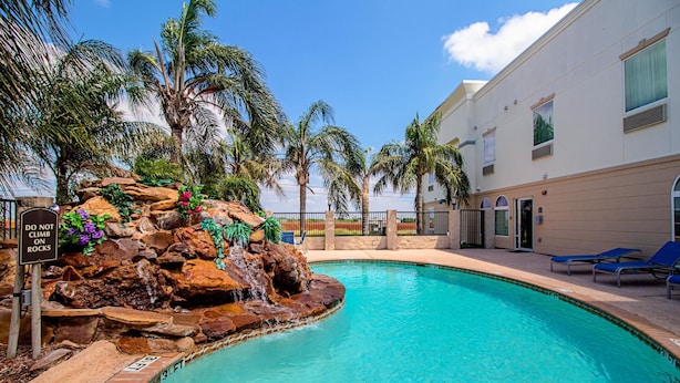 A swimming pool with a rock waterfall, palm trees, and lounge chairs.