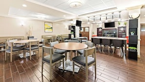 A modern dining area with round tables and chairs, a kitchen in the background, and a ceiling with recessed lighting.