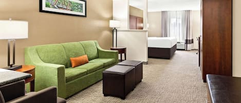 Una camera d'hotel con un divano verde, un tavolino, un poggiapiedi scuro, un letto e un grande specchio.