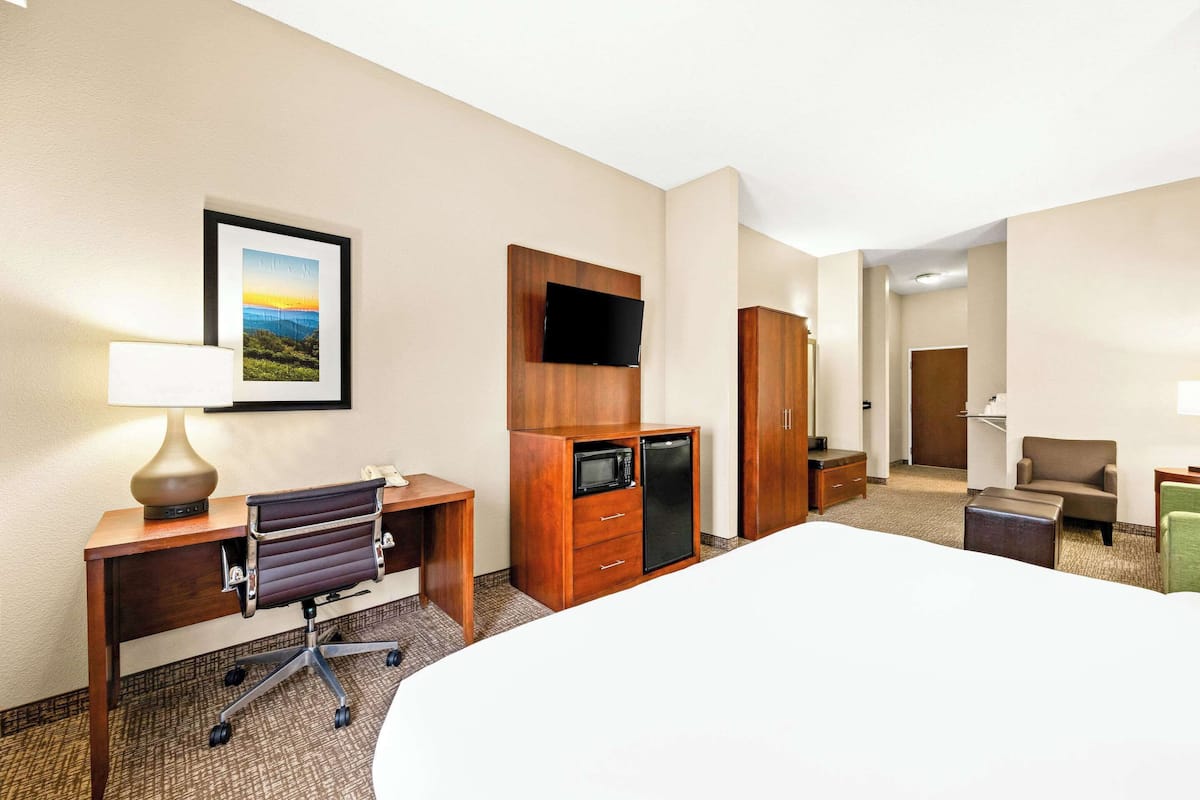 Quarto de hotel com cama, escrivaninha, cadeira, guarda-roupa, televisão e um quadro na parede.