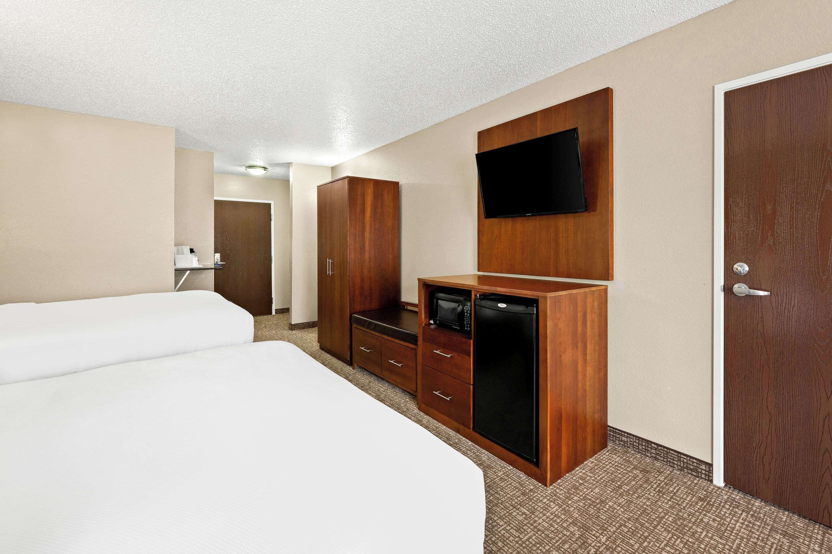 A hotel room with two beds, a wooden wardrobe, a flat-screen TV, and a door.
