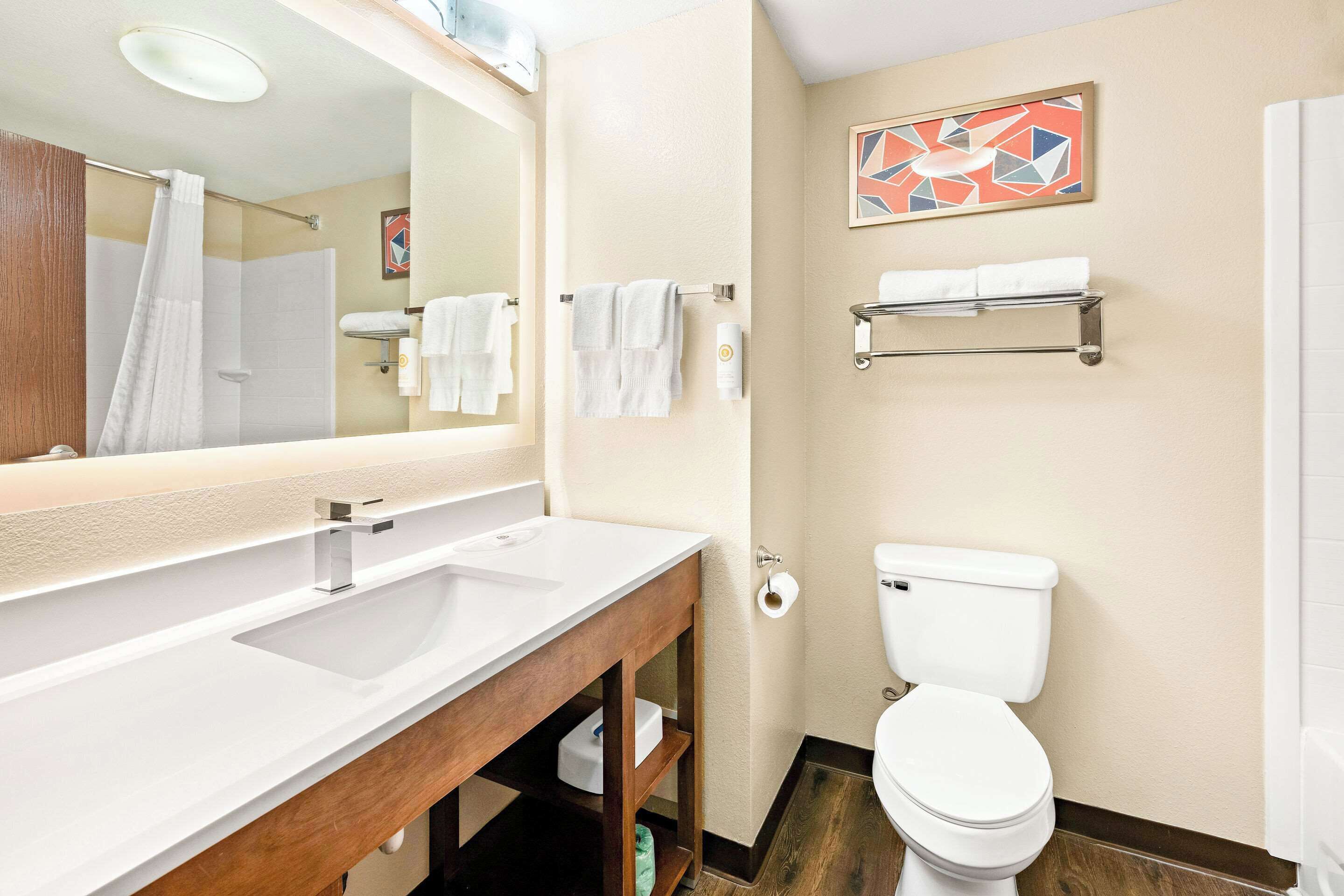 A modern bathroom with a white sink, mirror, and toilet. There are towels on a rack and a shower curtain visible.
