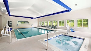 An indoor swimming pool with two separate sections, a changing room, and a view of the outdoors through large windows.