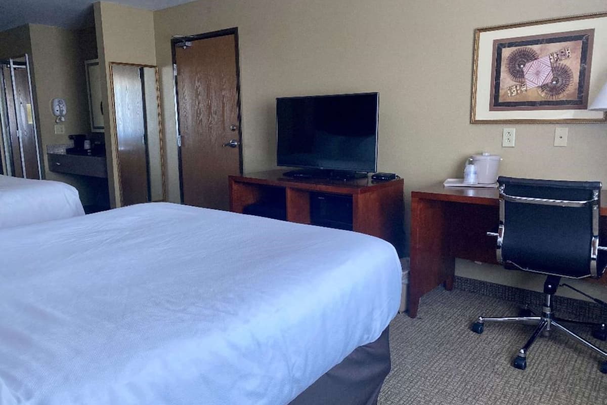 A hotel room with two beds, a TV, a desk with a chair, and a painting on the wall.