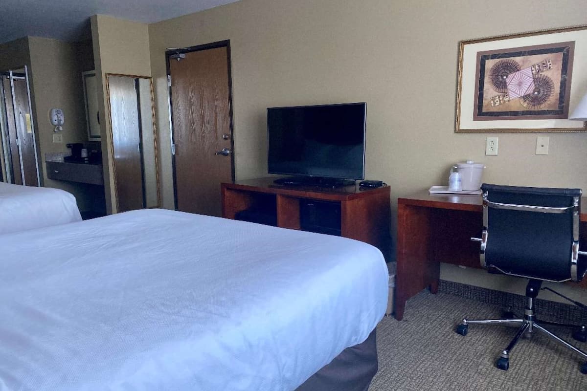 A hotel room with two beds, a television, a desk with a chair, and a framed picture on the wall.