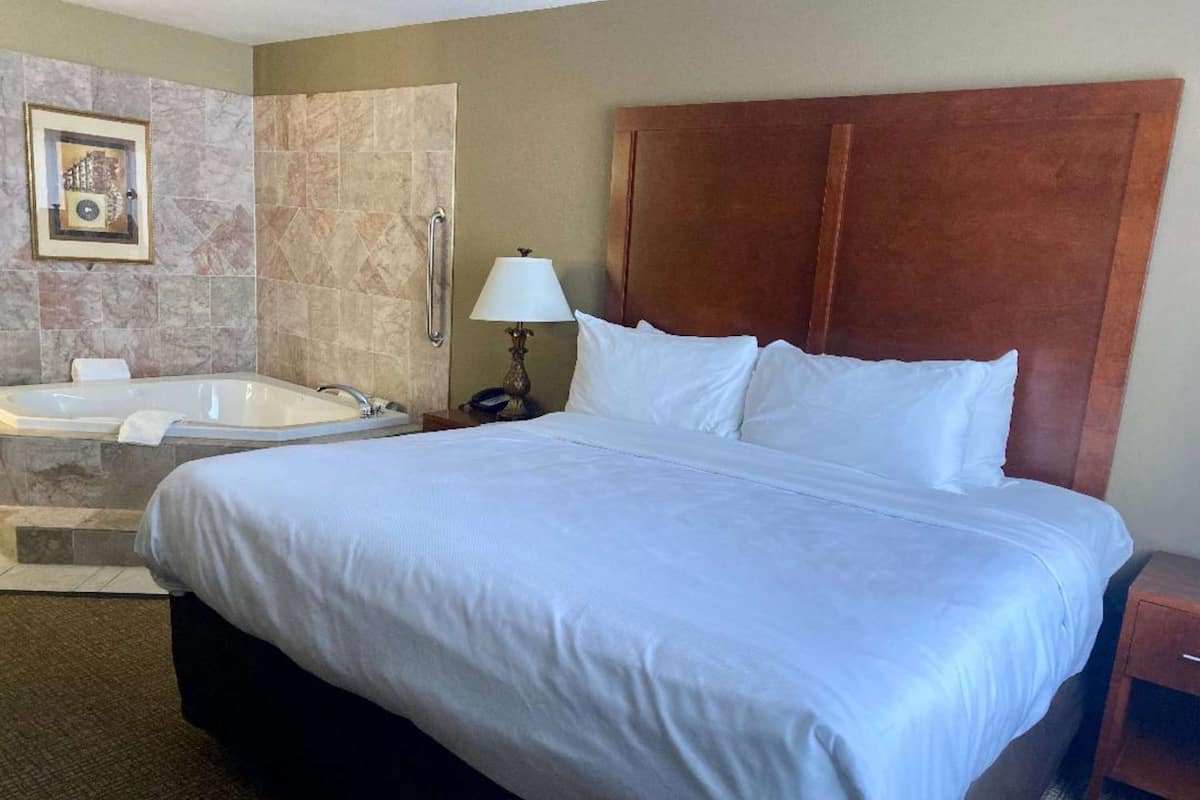 A hotel room with a large bed, a separate shower area, a bathtub, and a wooden headboard.