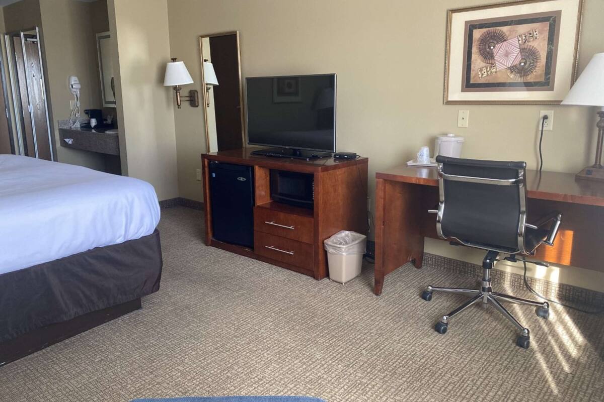 A hotel room with a bed, a desk with a computer, a chair, a TV, and a trash bin.
