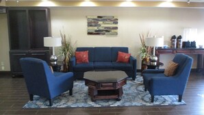 A living room with a blue sofa set, two armchairs, a coffee table, and a rug. There is a painting on the wall and a kitchen area in the background. - Best Western Emporia Inn (Emporia)