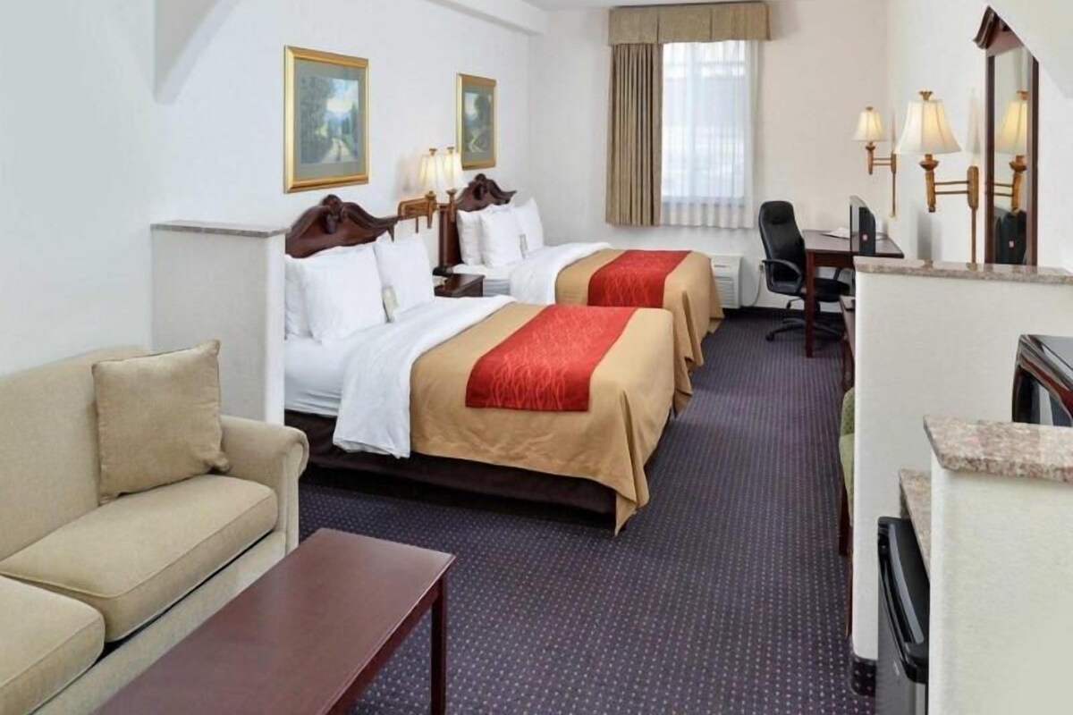 A hotel room with two beds, a desk, a chair, a sofa, and a mirror.